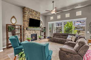 Living area featuring a ceiling fan, a stone fireplace, wood finished floors, baseboards, and a textured ceiling