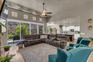 Living room with ceiling fan, a high ceiling, light wood finished floors, a textured ceiling, and a chandelier