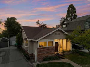 View of front facade featuring concrete driveway, an outbuilding, roof with shingles, and a garage
