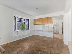 Kitchen featuring freestanding refrigerator, stone finish flooring, light countertops, brown cabinets, and a breakfast bar
