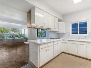 Kitchen featuring a sink, under cabinet range hood, white cabinetry, and light countertops