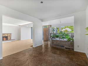 Unfurnished room with stone finish floors, baseboards, and a lit fireplace