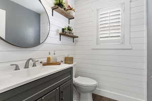 Bathroom featuring toilet, wood finished floors, vanity, and wooden walls