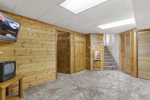 Finished basement with carpet flooring, a drop ceiling, wood walls, and stairway