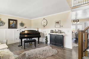 Sitting room with a decorative wall, a chandelier, crown molding, wood finished floors, and a wainscoted wall