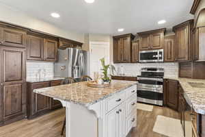 Kitchen featuring appliances with stainless steel finishes, light wood finished floors, a breakfast bar, a kitchen island, and light stone counters