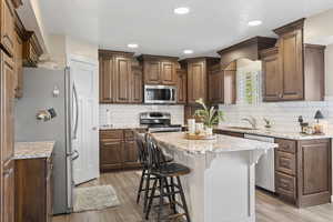 Kitchen with stainless steel appliances, a kitchen bar, light wood finished floors, a sink, and recessed lighting
