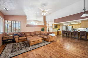 Living room with hardwood / wood-style floors, a ceiling fan, vaulted ceiling, and a textured ceiling