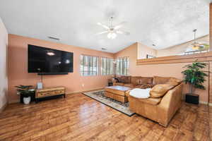 Living area featuring a ceiling fan, wood finished floors, vaulted ceiling, baseboards, and a textured ceiling