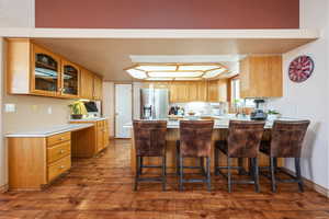 Kitchen featuring stainless steel refrigerator with ice dispenser, glass insert cabinets, dark wood-style floors, a peninsula, and a sink