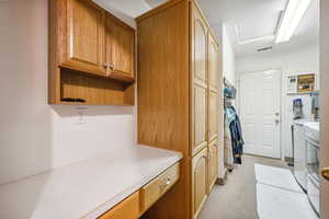 Clothes washing area with cabinet space, washing machine and dryer, and light colored carpet