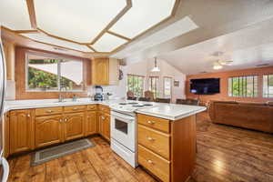 Kitchen with white electric stove, a peninsula, a sink, light countertops, and hardwood / wood-style flooring