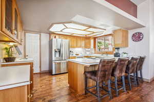 Kitchen featuring stainless steel fridge, a peninsula, wood finished floors, and light countertops