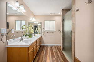 Bathroom with wood finished floors, a shower stall, baseboards, double vanity, and a textured ceiling