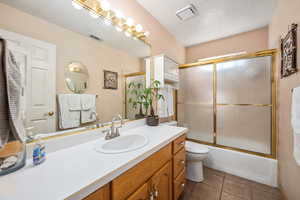 Bathroom featuring vanity, a textured ceiling, combined bath / shower with glass door, toilet, and tile patterned flooring