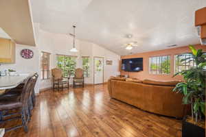 Living room featuring wood-type flooring, lofted ceiling, a ceiling fan, a textured ceiling, and baseboards
