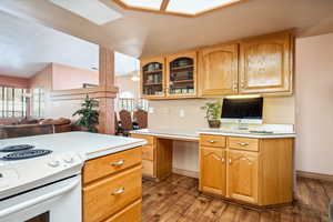 Kitchen with vaulted ceiling, white range with electric cooktop, wood finished floors, light countertops, and glass insert cabinets