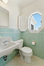 Bathroom featuring tile walls, toilet, tile patterned floors, a sink, and wainscoting