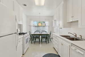 Kitchen featuring white appliances, a sink, white cabinets, and light countertops