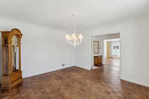 Unfurnished dining area featuring a chandelier, baseboards, and crown molding