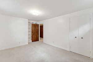 Unfurnished bedroom featuring a closet, light colored carpet, and baseboards