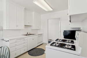 Kitchen featuring white appliances, a sink, white cabinetry, and light countertops