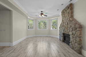 Unfurnished living room with ceiling fan, light wood-style flooring, baseboards, a fireplace, and crown molding