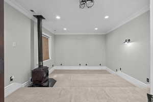 Basement featuring a wood stove, recessed lighting, carpet flooring, crown molding, and baseboards
