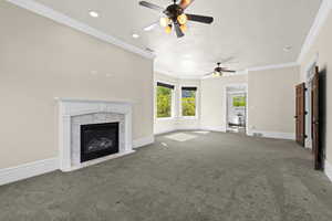 Unfurnished living room with ceiling fan, a high end fireplace, carpet floors, baseboards, and ornamental molding