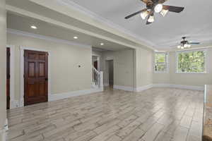 Spare room featuring a ceiling fan, stairway, light wood-type flooring, crown molding, and baseboards