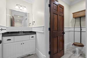 Bathroom with ornamental molding, wainscoting, a decorative wall, vanity, and marble finish floors