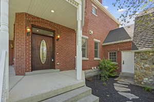 Property entrance featuring brick siding, a shingled roof, and a porch