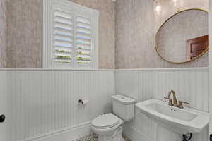 Half bathroom with wainscoting, toilet, a sink, and wallpapered walls
