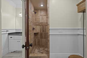Full bathroom featuring a tile shower, ornamental molding, vanity, and marble look tile flooring