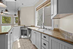 Kitchen with a sink, appliances with stainless steel finishes, ornamental molding, ceiling fan, and light stone countertops