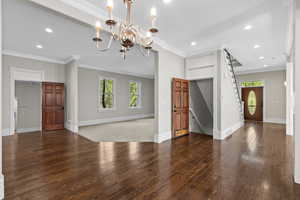 Unfurnished living room featuring wood-type flooring, recessed lighting, baseboards, a chandelier, and ornamental molding