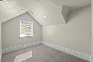 Bonus room featuring a textured ceiling, carpet, lofted ceiling, and baseboards