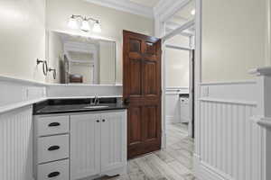 Bathroom featuring crown molding, a wainscoted wall, vanity, and a decorative wall