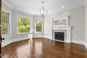 Unfurnished living room featuring a chandelier, wood-type flooring, plenty of natural light, crown molding, and baseboards