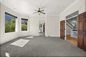 Empty room with plenty of natural light, crown molding, a ceiling fan, carpet, and baseboards