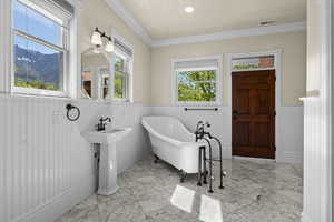 Full bath with wainscoting, marble finish floors, a freestanding tub, crown molding, and a mountain view