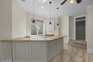 Kitchen with crown molding, baseboards, a sink, light stone counters, and a ceiling fan