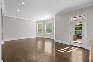 Unfurnished living room with recessed lighting, hardwood / wood-style floors, baseboards, ornamental molding, and a textured ceiling