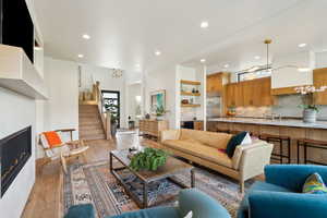 Living area featuring recessed lighting, stairway, a warm lit fireplace, and light wood-style floors