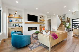 Living area featuring light wood-style flooring, stairs, a glass covered fireplace, recessed lighting, and built in features