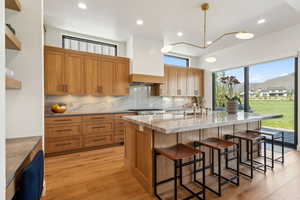 Kitchen with decorative backsplash, a sink, a kitchen island with sink, a breakfast bar area, and light stone countertops