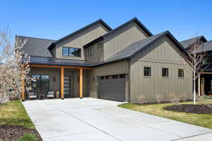 Modern inspired farmhouse with roof with shingles, driveway, board and batten siding, and an attached garage