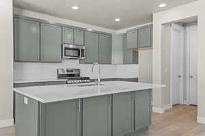 Kitchen with gray cabinetry, decorative backsplash, appliances with stainless steel finishes, light wood-type flooring, and recessed lighting