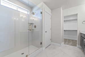 Full bath featuring a stall shower, vanity, light marble finish floors, and a spacious closet