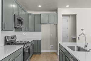 Kitchen with stainless steel appliances, light wood-style flooring, tasteful backsplash, a textured ceiling, and light stone countertops